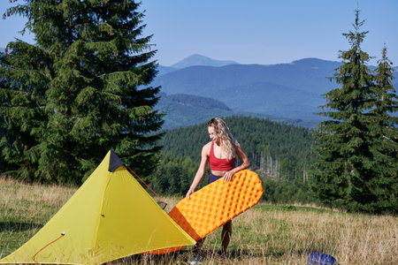 Woman hiker camping in mountains. Woman hiking, traveling in hot summer morning outdoors. Slim female holding rubber mattress, enjoying landscape. Concept of tourism and adventure.の写真素材