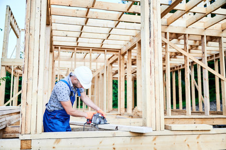 Carpenter using circular saw for cutting wooden plank. Man worker building wooden frame house. The idea behind modern ecological construction.の写真素材