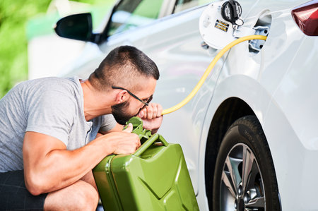 Weird man pumping gasoline from a gas tank into canister. Self-confident thief stealing fuel in broad daylight. Male adult trying to pump fuel from tank by hose.の写真素材