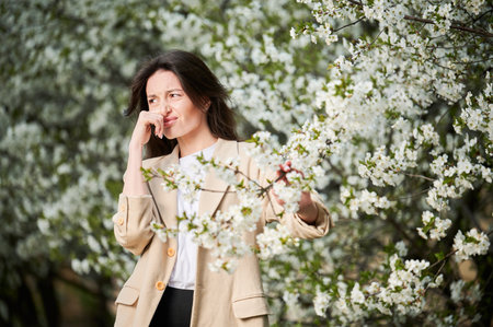 Woman allergic suffering from seasonal allergy at spring in blossoming garden at springtime. Young woman sneezing, having runny nose in front of blooming tree. Spring allergy conceptの写真素材