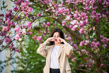 Woman allergic suffering from seasonal allergy at spring in blossoming garden at springtime. Young woman sneezing, closing nose by hands in front of blooming tree. Spring allergy conceptの写真素材