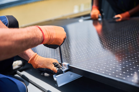 Worker building photovoltaic solar panel system on rooftop of house. Close up of man engineer in gloves installing solar module with help of hex key outdoors. Alternative energy generation concept.の写真素材