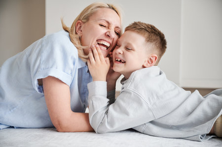 Joyful mom laughing with her son. Lovely moment of young mother and her kid smiling at home. Happy child having fun with his parent.の写真素材