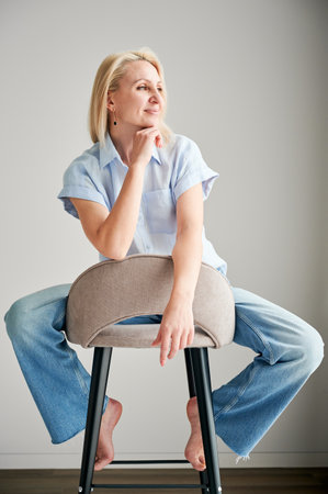 Pretty female relaxing on bar stool. Woman with blonde hair looking away. Beautiful woman sitting on bar stool in her apartment.の写真素材