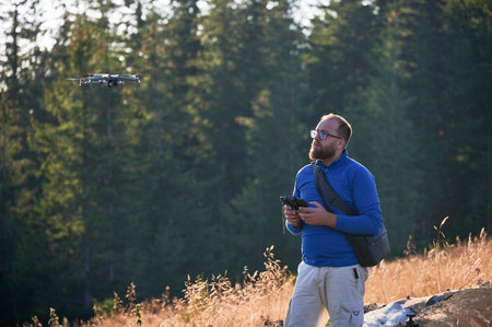 Professional photographer taking photos from drone. Young man taking aerial photos in mountains. Man controlling his drone on background of mountain forest.の写真素材