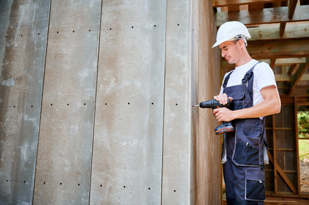 Carpenter constructing wooden framed house. Man worker cladding facade of house with cement particle boards, fastening them with screwdriver. Concept of modern eco-friendly construction.の写真素材