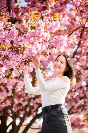 Woman allergic enjoying after treatment from seasonal allergy at spring. Portrait of happy beautiful woman smiling in front of blooming sakura tree at springtime. Spring allergy concept.の写真素材