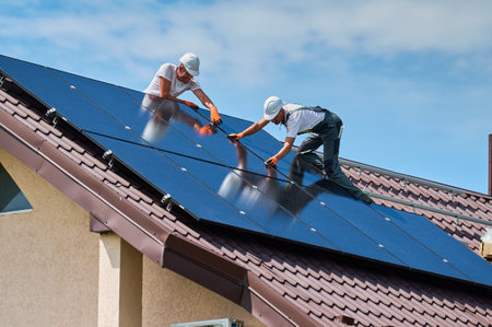 Workers building solar panel system on rooftop of house. Two men installers in helmets installing photovoltaic solar module outdoors. Alternative, green and renewable energy generation concept.の写真素材