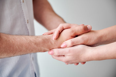 Close up of two hands engaging in delicate touch. Mans and womans hands on white neutral background. Husband holding hand of his lovely wife. Concept of affection, support, and mutual respect.の写真素材