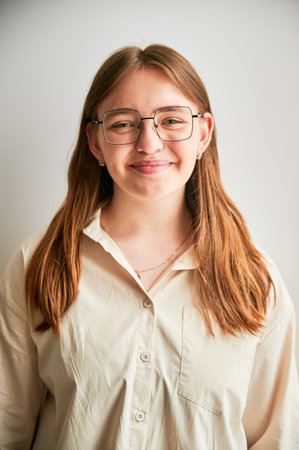 Portrait of beautiful girl smiling to camera. Cute girl in cream shirt and square glasses posing on white background.の写真素材