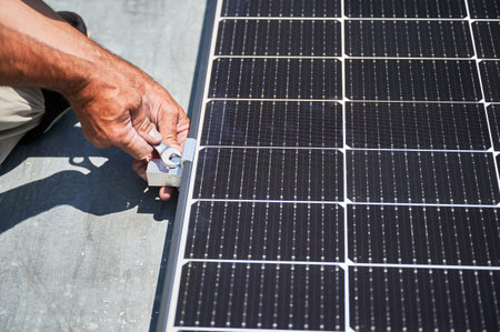 Worker building photovoltaic solar panel system on rooftop of house. Close up of man engineer installing solar module with help of wrench outdoors. Alternative and renewable energy generation concept.の写真素材