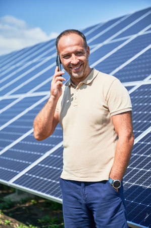 Happy businessman having important call. Man talking about his investment in alternative energy resource. Man taking on phone on background of solar panels.の写真素材