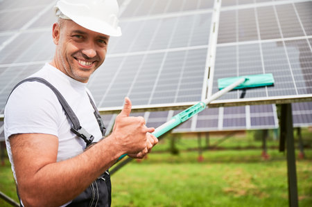 Professional worker showing his good job of cleaning solar panel. Enthusiastic man smiling to camera and showing thumbs up. Young male wiping energy resource from dirt.の写真素材