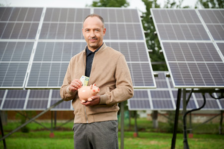 Confidence man putting earned money to piggy bank. Male adult saving profit he got from investing in green energy. Man in casual clothes holding moneybox and putting euros in it.の写真素材