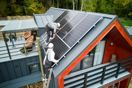 Technicians building photovoltaic solar module station on roof of house. Men roofers in helmets installing solar panel system outdoors. Concept of alternative and renewable energy. Aerial view.の写真素材