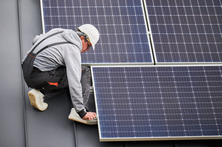 Man worker mounting photovoltaic solar panels on roof of house. Engineer in helmet installing solar module system with help of hex key. Concept of alternative, renewable energy.の写真素材