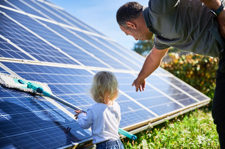 Man showing his small child the solar panels during warm day. Cute boy cleaning solar battery together with his dad. Young father teaching little son how to care about their source of energy.の写真素材