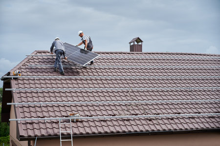 Men technicians carrying photovoltaic solar modul on roof of house. Builders in helmets building solar panel system outdoors. Concept of alternative and renewable energy.の写真素材