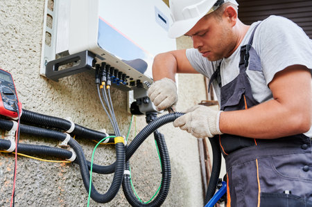Man electrician installing solar panel system. Technician in helmet and gloves making electrical wiring inverter and electric box. Concept of alternative and renewable energy.の写真素材