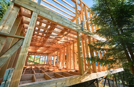 Under-construction residential wooden frame home located near a forest. Commencement of a new construction project for a cozy house or a mountain cottage. Idea of contemporary ecological construction.の写真素材