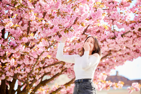 Woman allergic suffering from seasonal allergy at spring in blossoming garden at springtime. Young woman having runny nose in front of blooming tree. Spring allergy conceptの写真素材