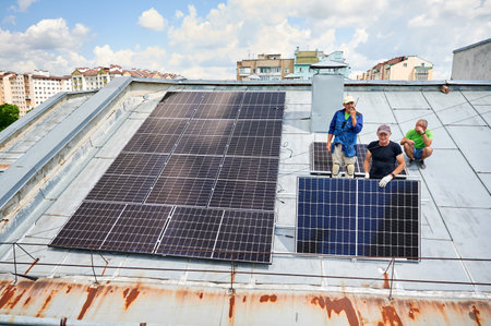 Workers building solar panel system on metal rooftop of house. Three men installers installing photovoltaic solar module outdoors. Alternative, green and renewable energy generation concept.の写真素材