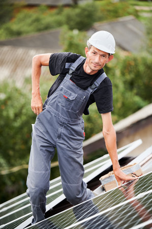 Portrait of man technician installing photovoltaic solar moduls on roof of house. Electrician in helmet building solar panel system outdoors. Concept of alternative and renewable energy.の写真素材