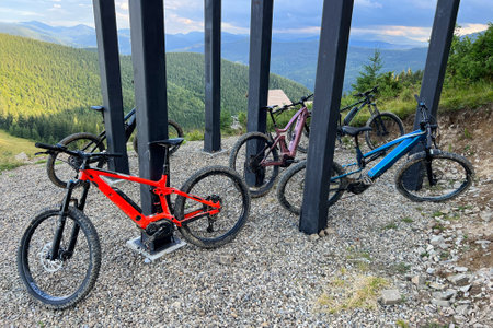 Collection of mountain electric bikes parked on a gravel-covered ground in the mountains. MTB bikes are placed under a structure with thick black pillars.の写真素材