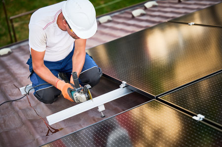 Worker installing or maintaining photovoltaic solar panel system on roof of house. Technician in helmet using grinder on metal part of the panels mounting structure. Concept renewable energy.の写真素材