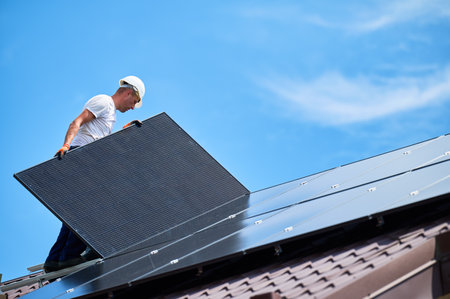 Workers building solar panel system on rooftop of house. Two men installers in helmets installing photovoltaic solar module outdoors. Alternative, green and renewable energy generation concept.の写真素材