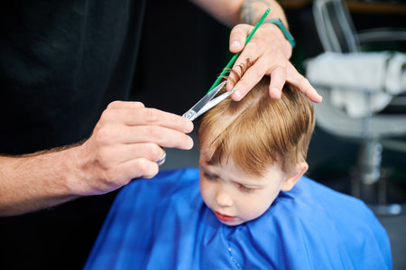 Cute boy worried about new haircut. Adorable client changing style. Cropped photo of barber cutting boys hair.の写真素材