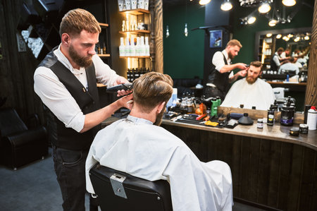 Professional barber using comb and electric shaver to cut side hair. Close-up view of male customer getting stylish haircut.の写真素材