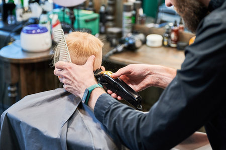 Barber using comb and shaver to cut hair. Professional hairdresser shaving little kids nape.の写真素材