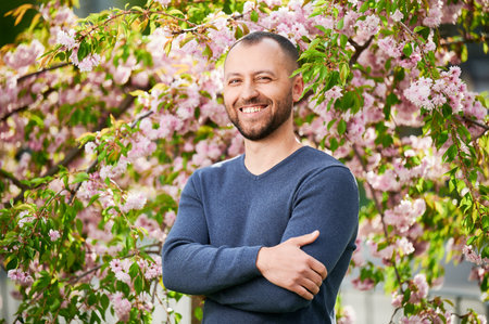 Man allergic enjoying after treatment from seasonal allergy at spring. Portrait of happy bearded man smiling in front of blossom tree at springtime. Spring allergy concept.の写真素材