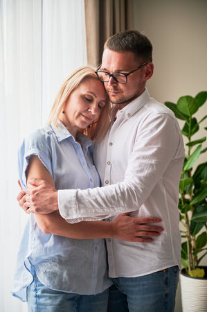 Happy couple hugging on light background at home. Pretty woman smiling and hugging her husband with closed eyes. Sweet couple in casual clothes.の写真素材