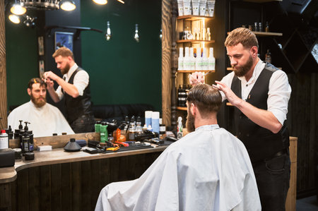 Confident man getting new hairstyle. Experienced barber cutting wet hair. Regular appointment in barbershop.の写真素材