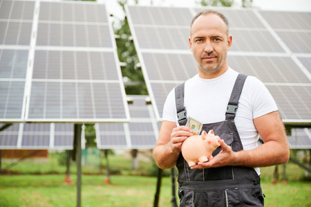 Man putting money in piggy bank on background of solar panels. Male adult making investment in future. Knowledgeable man investing in alternative energy sources.の写真素材