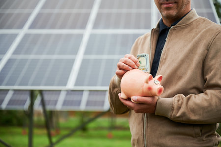 Man investing in ecological energy sources. Cropped view of investor putting his money in piggy bank. Investments in green energy concept.の写真素材