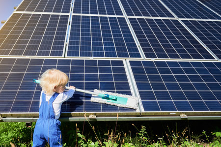 Small boy learning how to care about solar panels. Back view of young kid cleaning new solar battery at warm sunny day. Concept of young generation and alternative energy.の写真素材