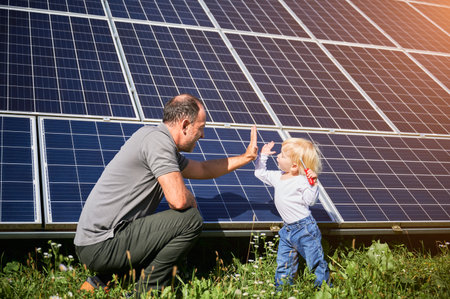 Little son and his happy father giving each other high-five on background of solar panels. Young father glad spending time with his child. Happy family of two on background of solar panels.の写真素材