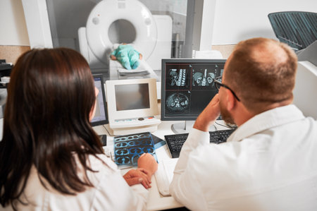 Medical computed tomography or MRI scanner. Back view of two doctors sitting, working at computer, making MRI. Two specialists consulting, talking, thinking, looking. Concept of modern diagnostics.の写真素材