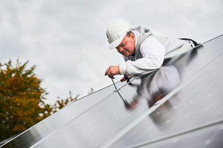 Man worker mounting photovoltaic solar panels on roof of house. Engineer in helmet installing solar module system with help of hex key. Concept of alternative, renewable energy.の写真素材