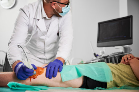 Male specialist examination of patients knee in his office, boy patient lying on coach. Doctor wearing white robe, latex gloves, glasses and mask. Concept of checkup and healthcare.の写真素材