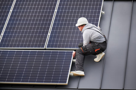 Engineer mounting photovoltaic solar panels on roof of house. Man technician in helmet installing solar modules system outdoors. Concept of alternative and renewable energy.の写真素材