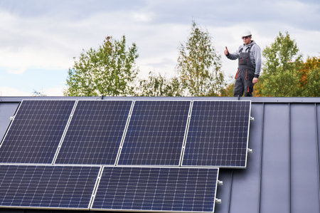 Portrait of man technician installing photovoltaic solar modules on roof of house, showing thumbs up. Electrician in helmet building solar panel system. Concept of alternative and renewable energy.の写真素材