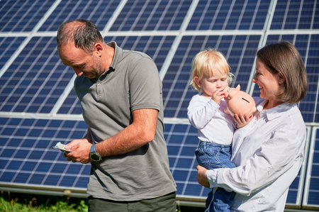 Happy parents investing into their child. Modern family glad to earn money for financial safety cushion. Man and his family counting money on background of solar panel.の写真素材