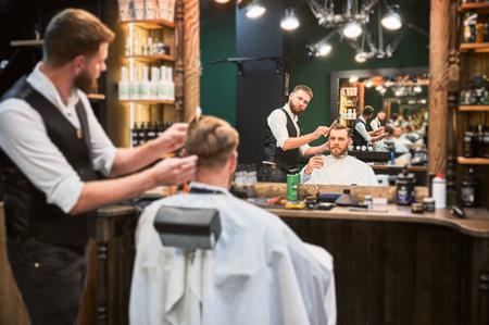 Regular client enjoying his drink while getting haircut. Professional hairdresser making stylish haircut, Luxury barbershop offering drink.の写真素材