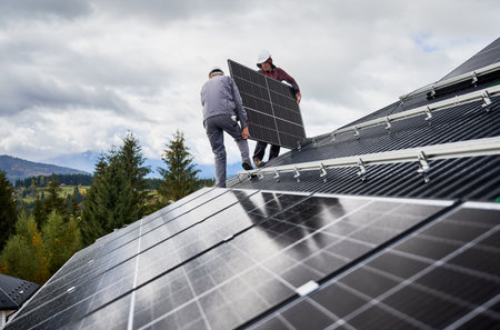 Electricians installing solar panel system on roof of house. Men workers in helmets carrying...