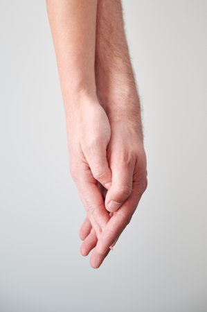 Close up view of hands of sweet couple. Young man and woman holding hands on light neutral background. Concept of love, intimacy, support, and trust.の写真素材