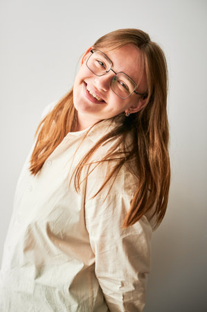 Portrait of beautiful girl smiling to camera. Cute girl in cream shirt and square glasses posing on white background.の写真素材